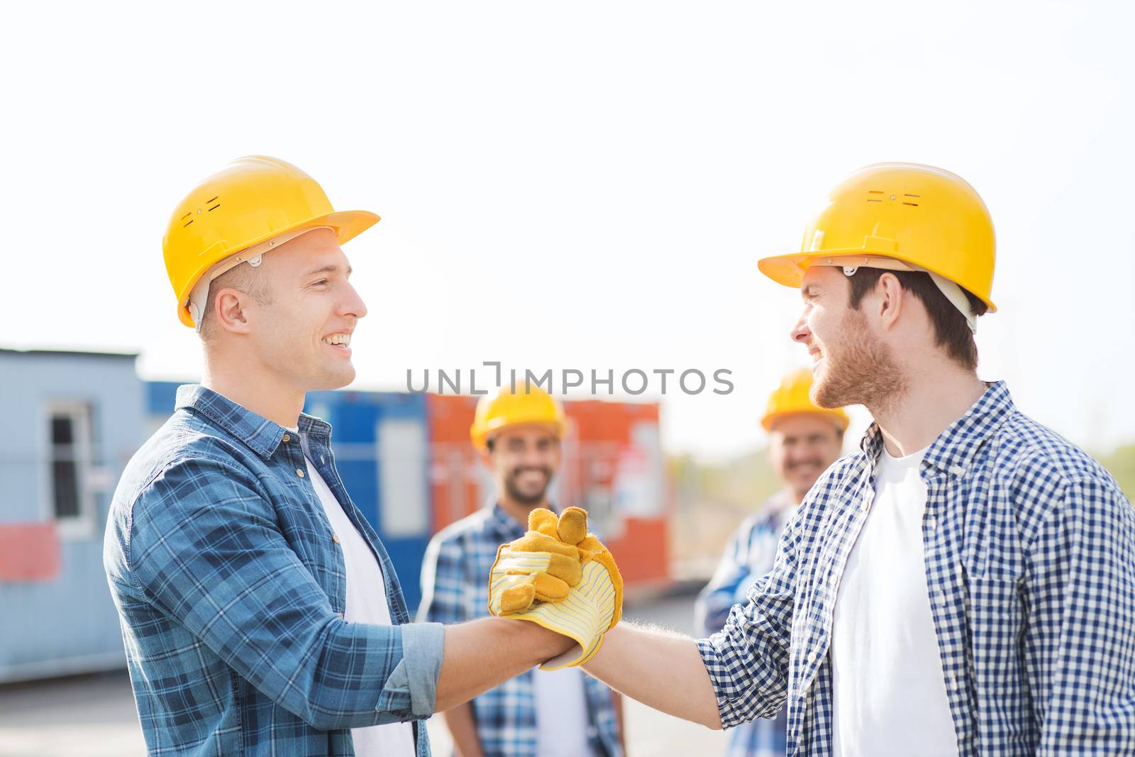 business, building, teamwork, gesture and people concept - group of smiling builders in hardhats greeting each other with handshake outdoors