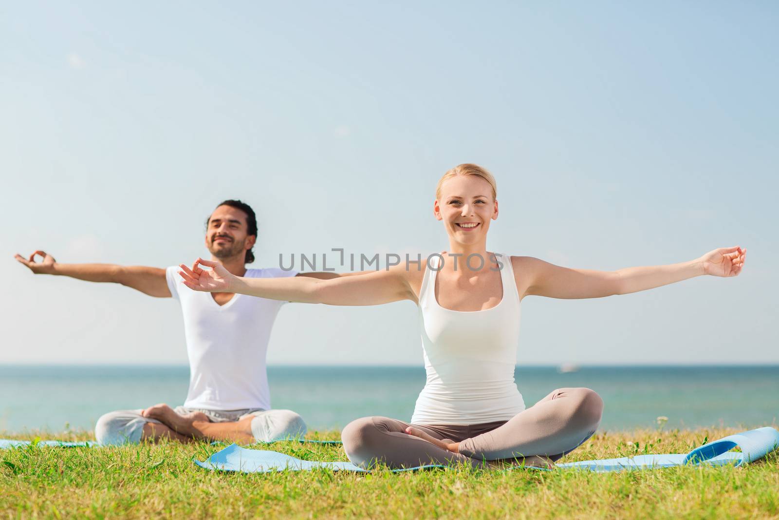 smiling couple making yoga exercises outdoors by dolgachov