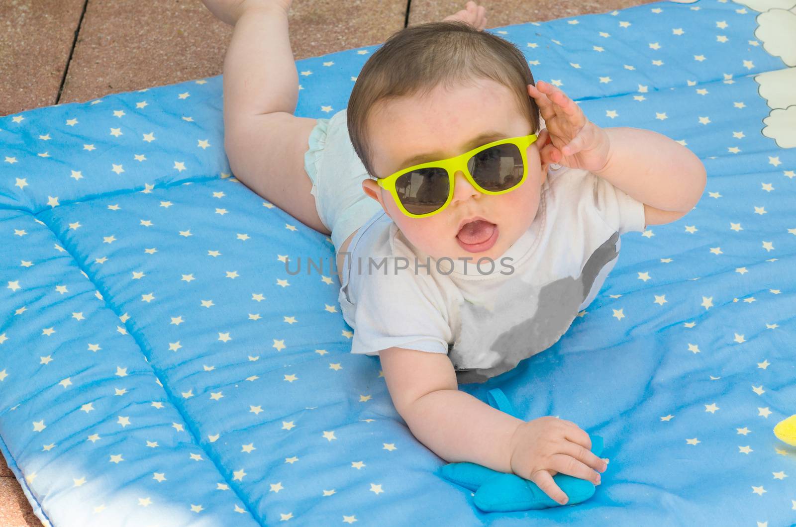 Baby posing on a blue blanket and wearing sun glasses.