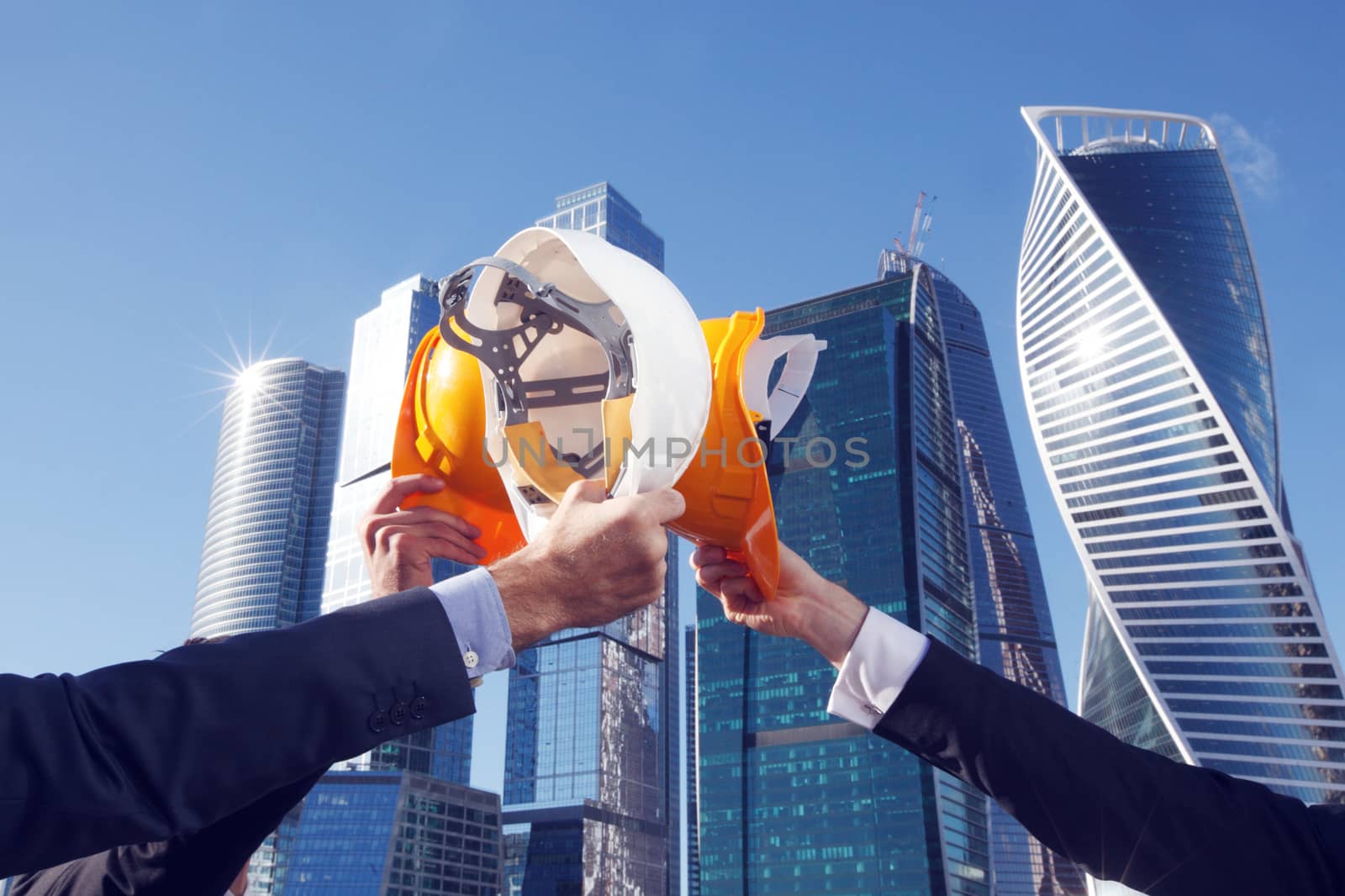 Group of business people clinking their helmets as a success on skyscrapers background, construction finished concept