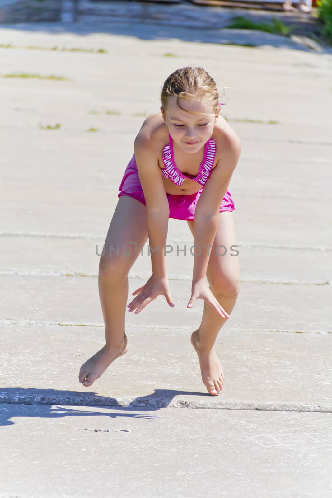 Cute jumping girl on the riverbank in pink swimsuit