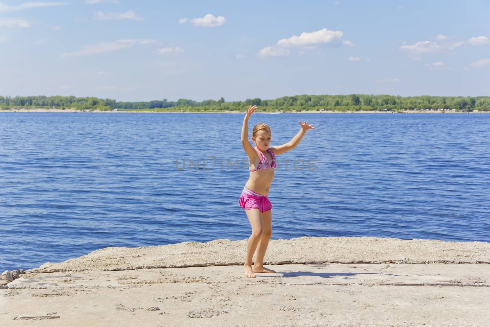 Dancing girl on the riverbank in pink swimsuit