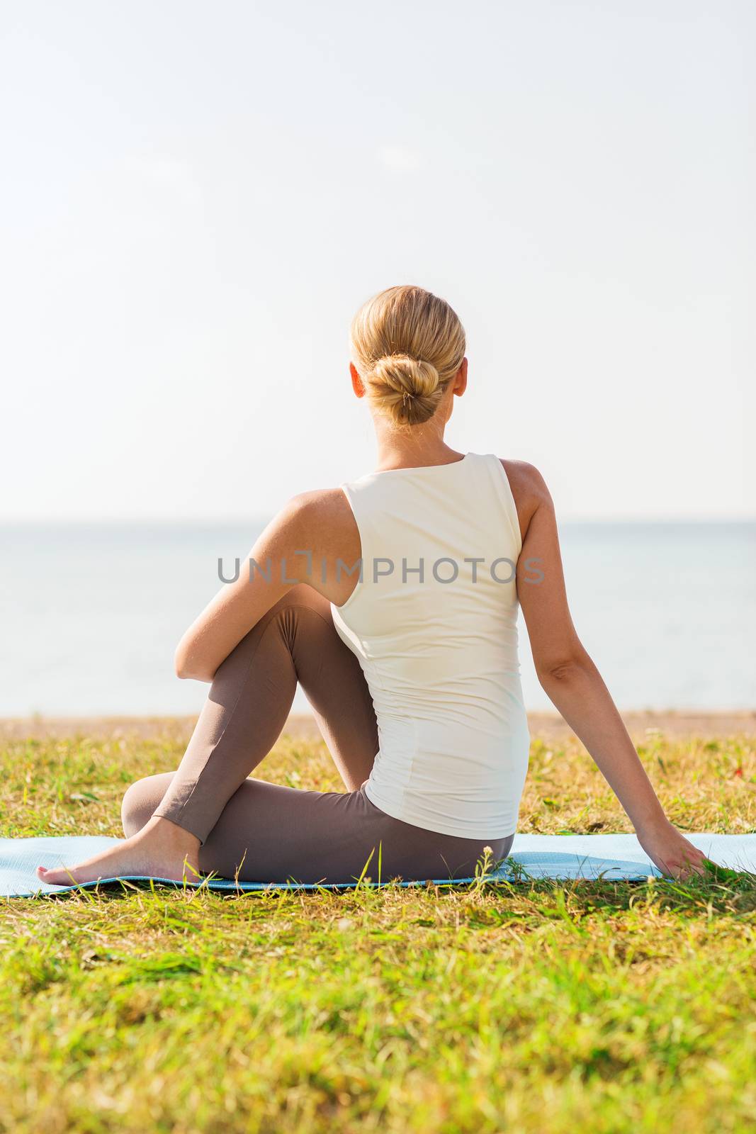 fitness, sport, people and lifestyle concept - woman making yoga exercises on mat outdoors from back