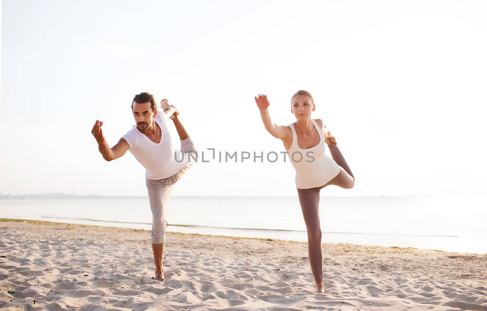 fitness, sport, friendship and lifestyle concept - couple making yoga exercises on beach