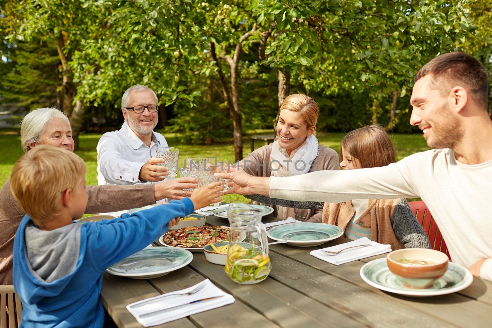 family, generation, home, holidays and people concept - happy family having dinner and clinking glasses in summer garden