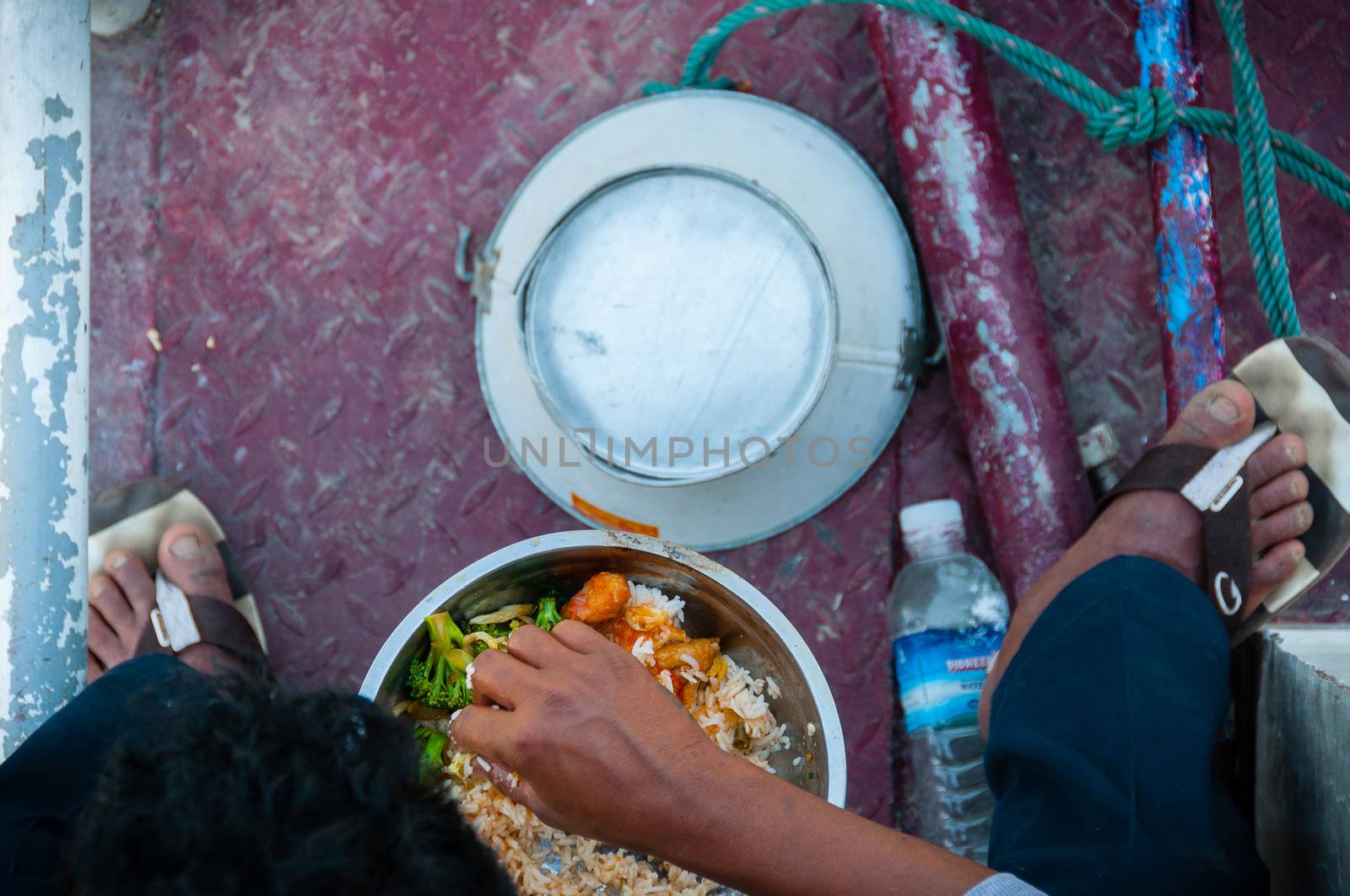 Asian man eating food from above sitting on a ship