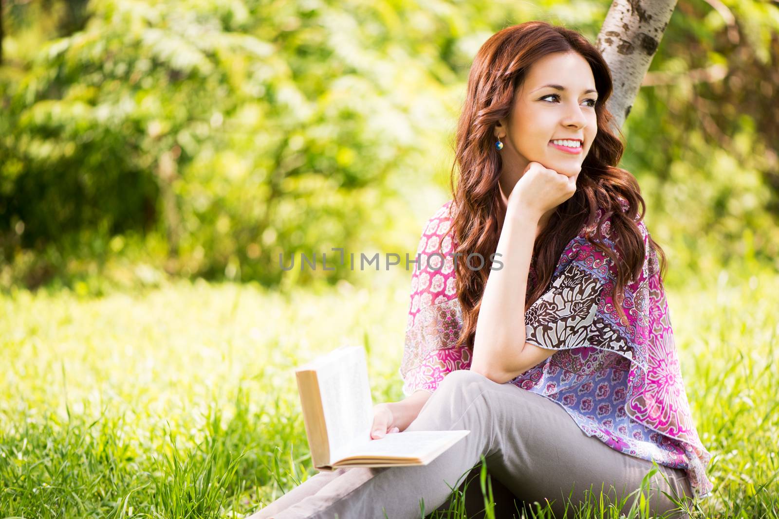 Beautiful Girl with a book in the park sitting on the grass and Expressing Positivity.