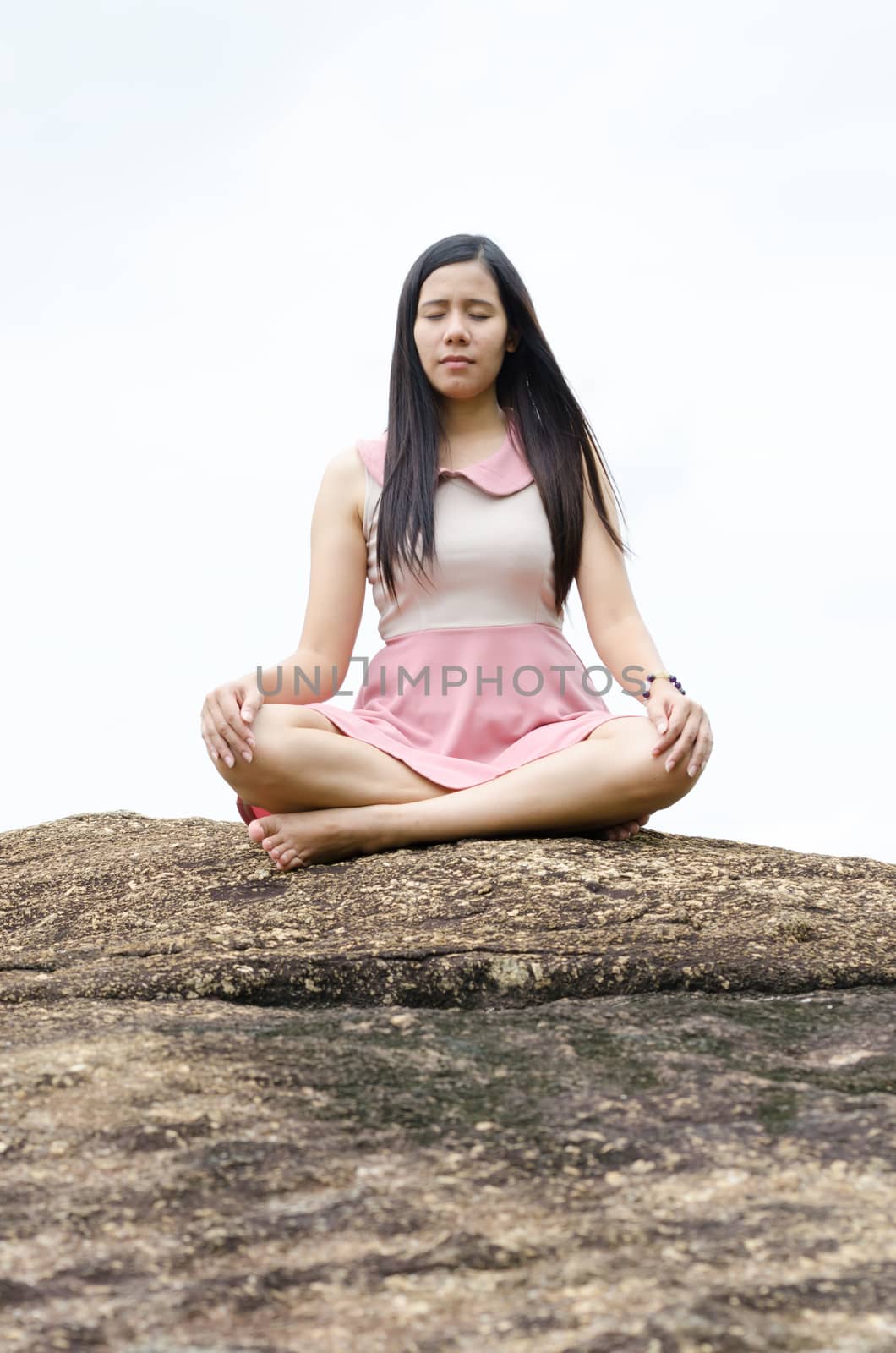 Woman Yoga meditation sitting on stones with mountains and white sky on background harmony with nature concept.