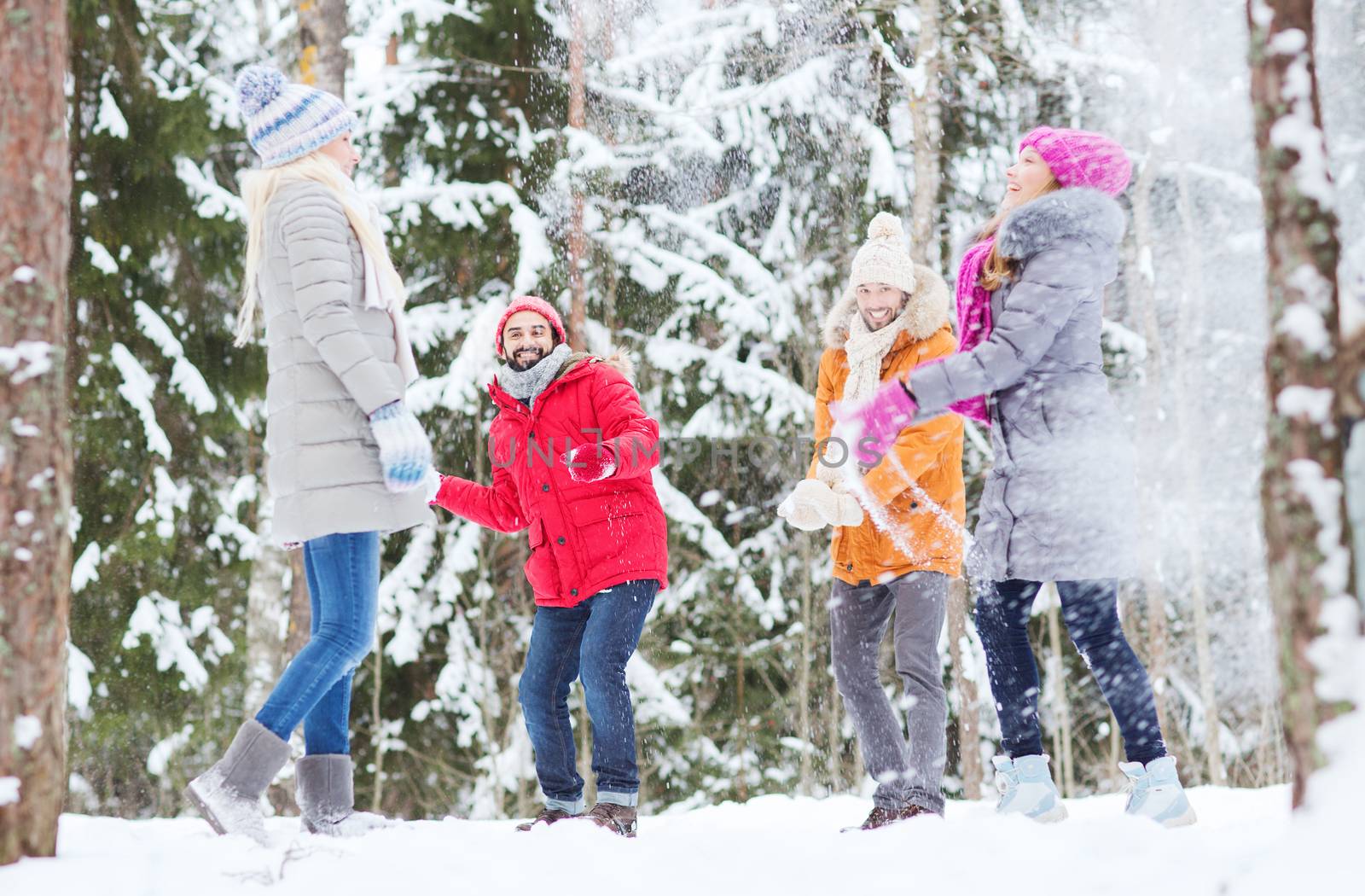 love, season, friendship, entertainment and people concept - group of happy men and women having fun and playing snowballs in winter forest