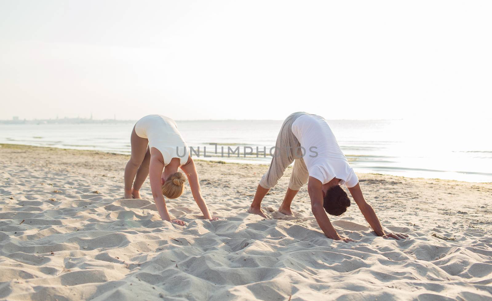 fitness, sport, friendship and lifestyle concept - couple making yoga exercises on sand outdoors