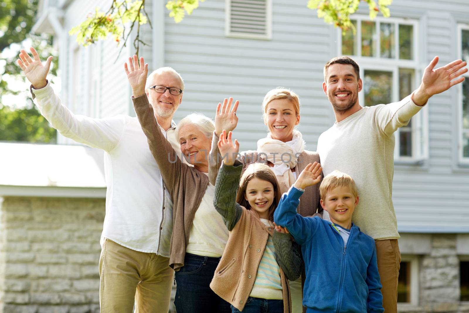 happy family waving hands in front of house by dolgachov