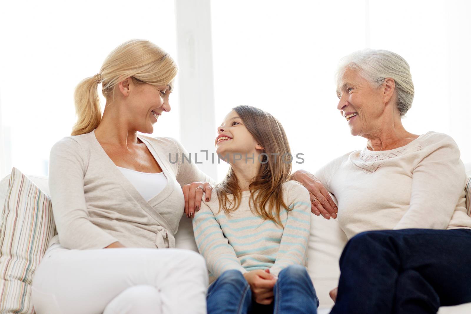 family, happiness, generation and people concept - smiling mother, daughter and grandmother sitting on couch at home