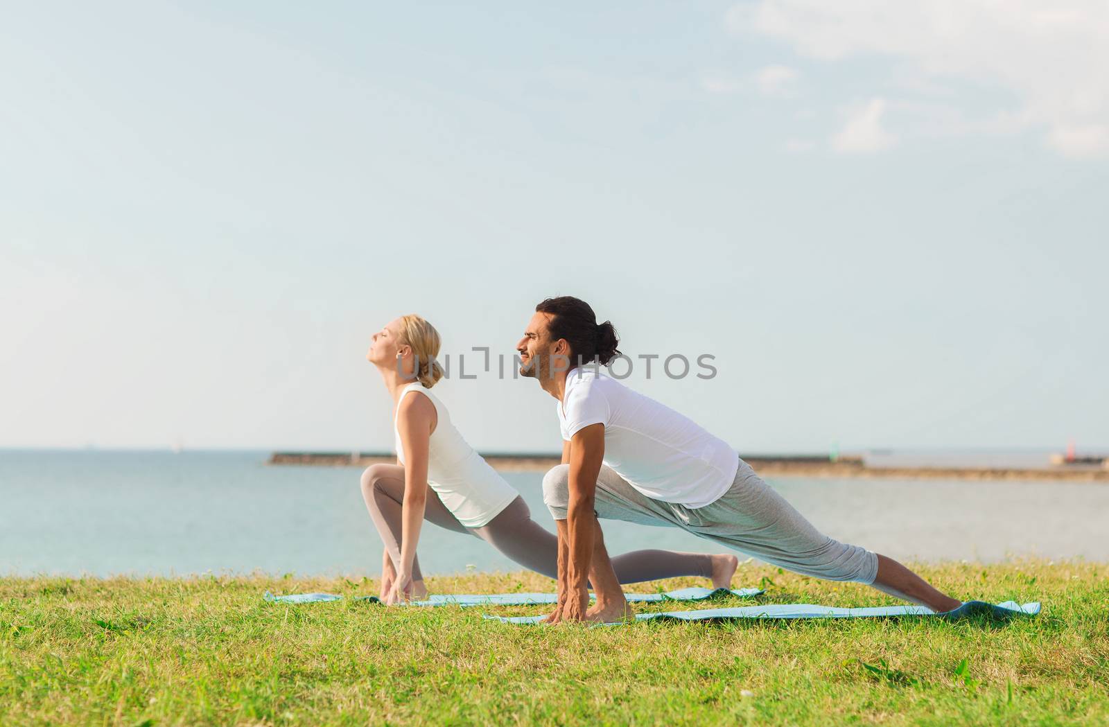 fitness, sport, friendship and lifestyle concept - smiling couple making yoga exercises on mats outdoors