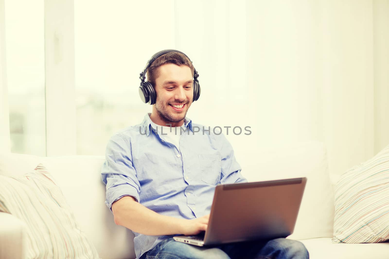 smiling man with laptop and headphones at home by dolgachov