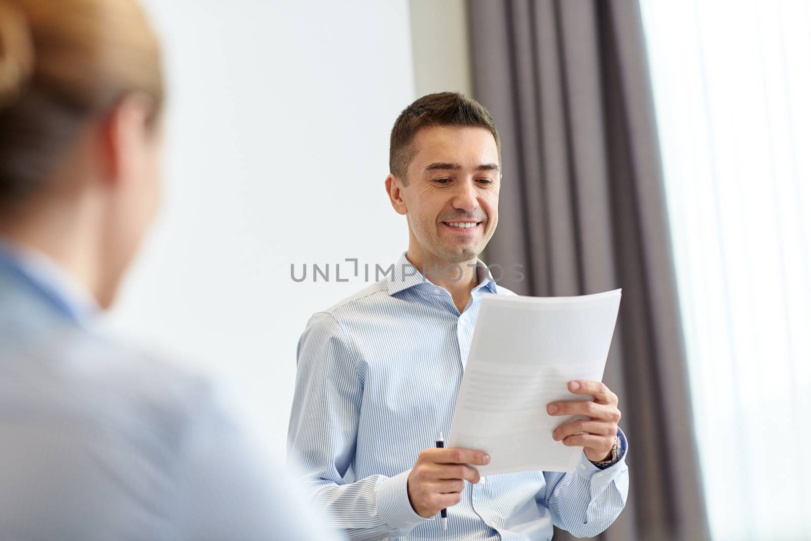 business, people and conference concept - smiling businessman holding and reading papers in office