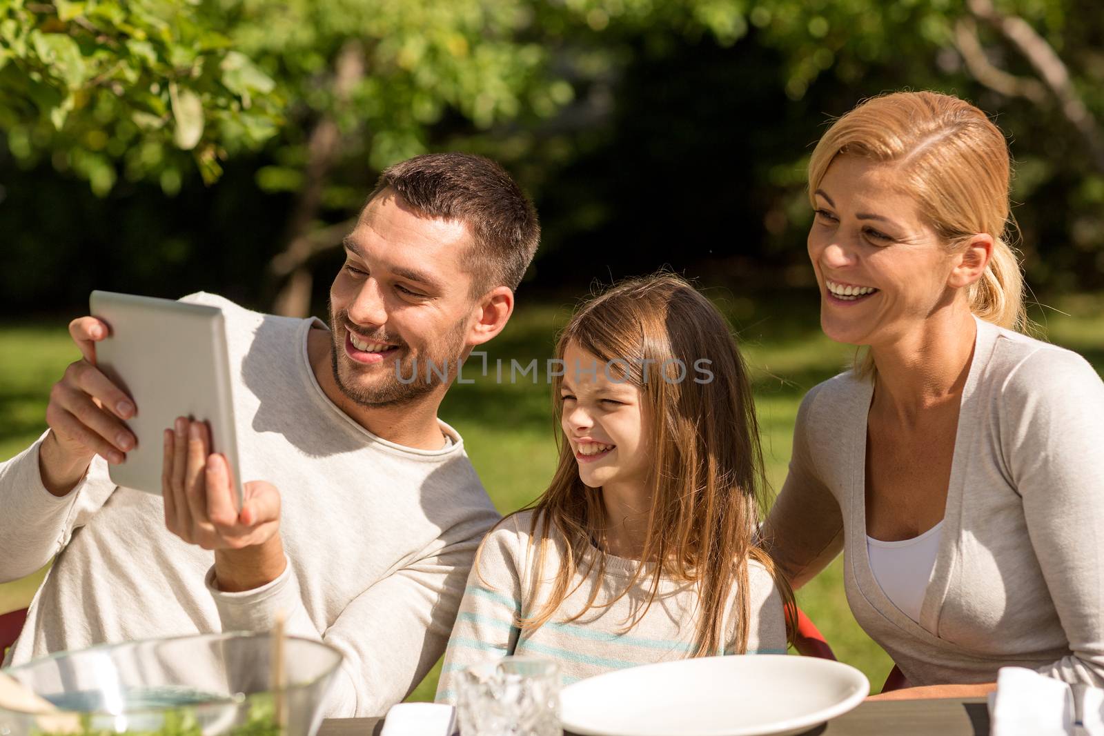 family, happiness, generation, home and people concept - happy family sitting at table and taking selfie with tablet pc computer outdoors