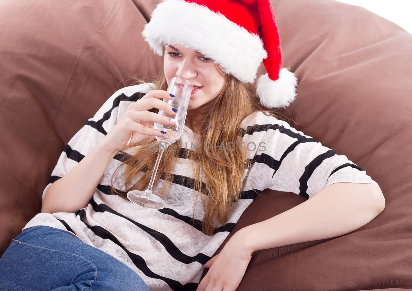 Cheerful girl in the Santa Claus hat. Girl sitting on a chair with a glass of champagne.