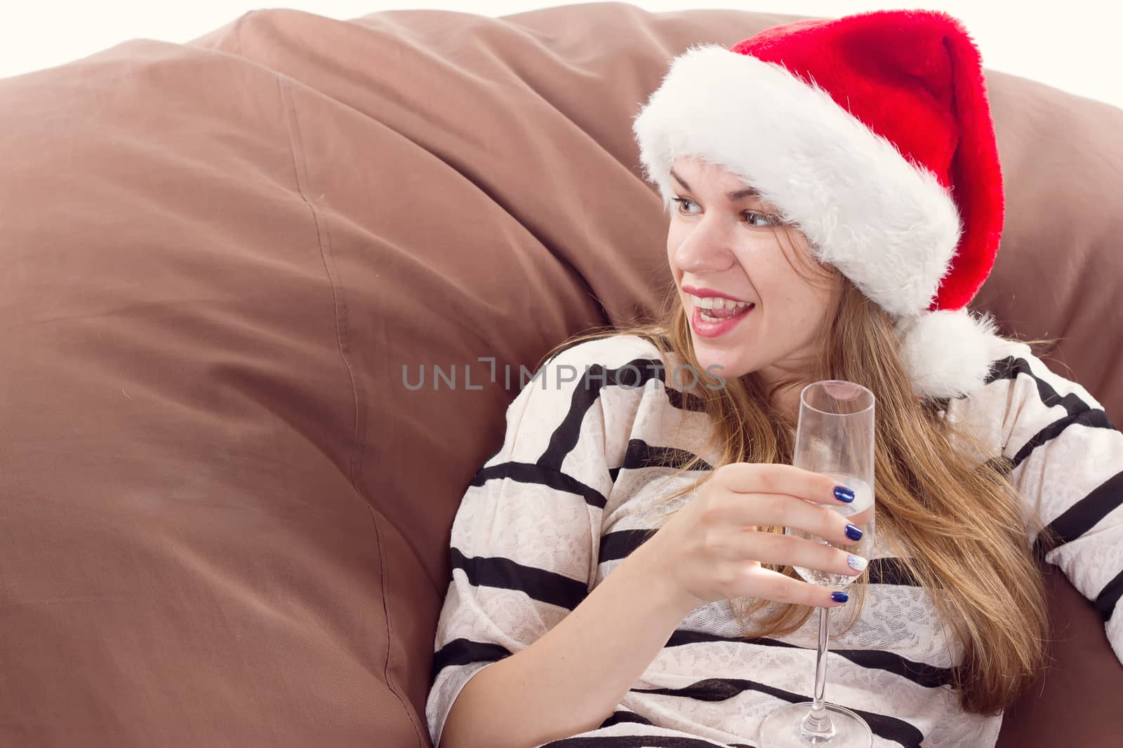 Cheerful girl in the Santa Claus hat. Girl sitting on a chair with a glass of champagne.