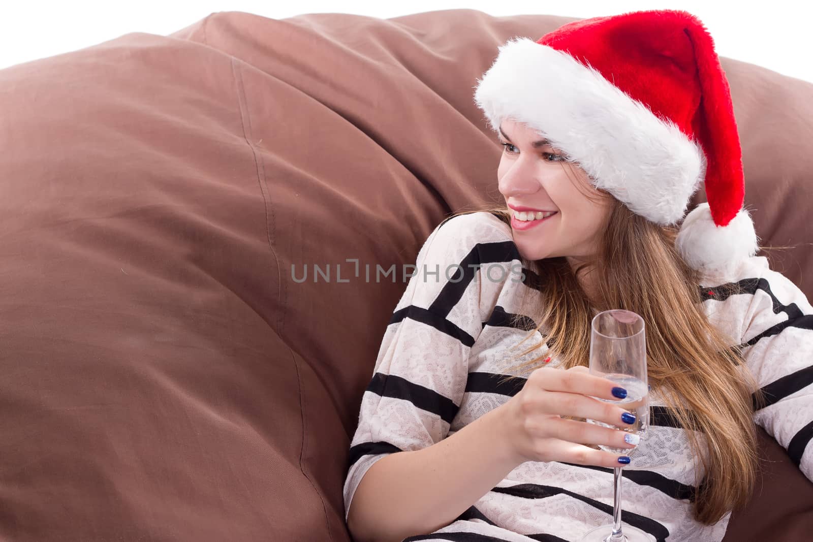 Cheerful girl in the Santa Claus hat. Girl sitting on a chair with a glass of champagne.