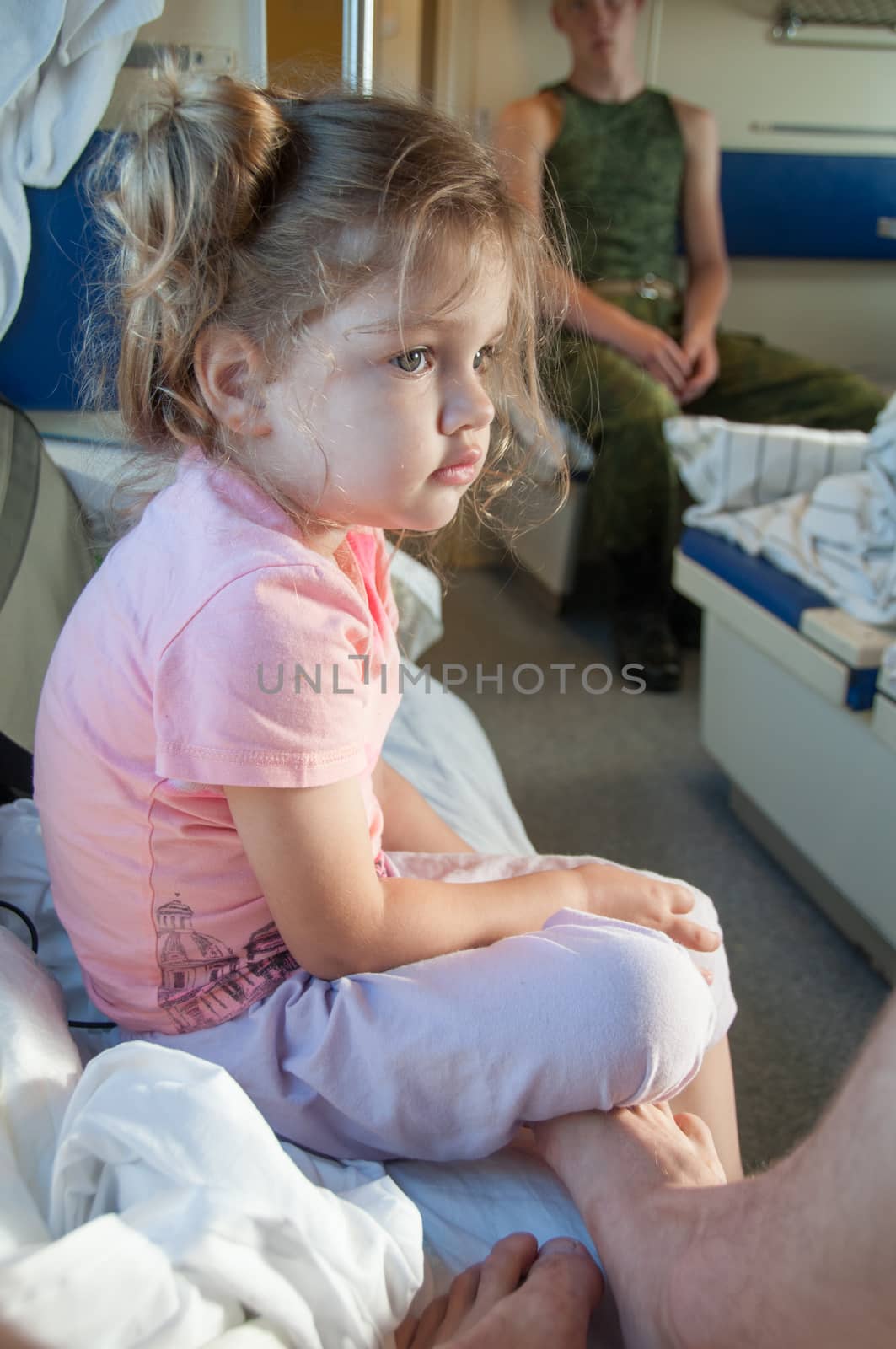 Sad three year old girl sitting on a bed in a second-class train carriage