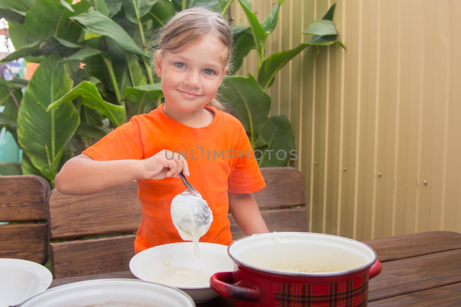 Four-year girl on breakfast imposes a ladle into a bowl semolina
