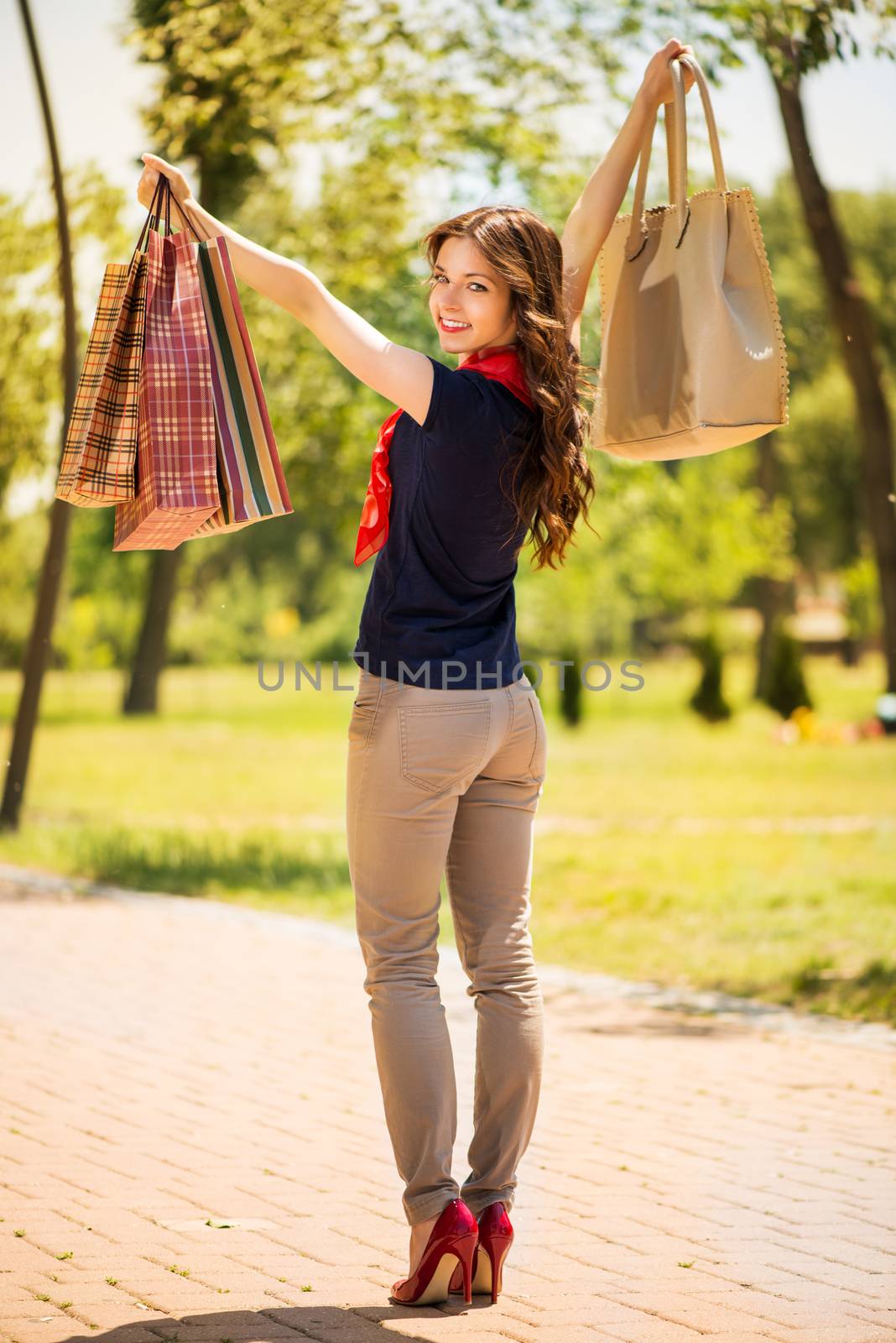 Beautiful young woman walking in the park and holding shopping bags.