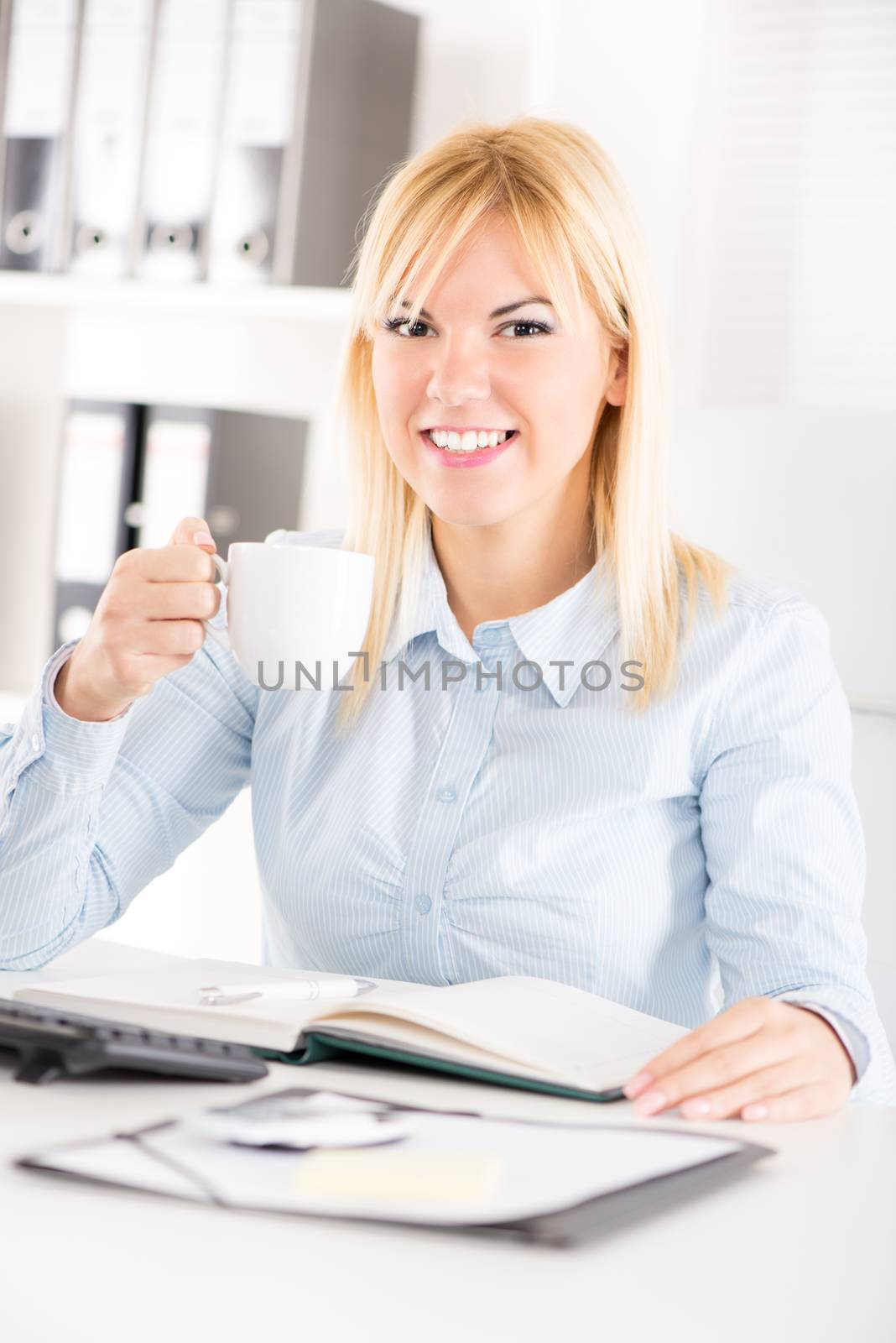 Businesswoman in the office having leisure time. Sitting at the table and drink coffee.