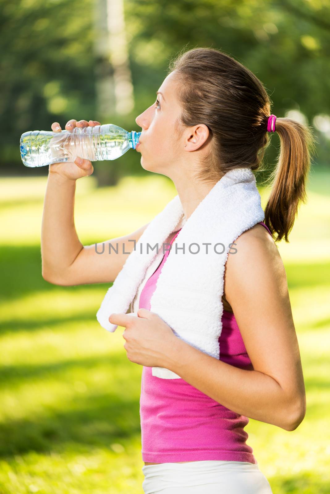 Beautiful young woman resting and drinking water after exercising in the park.