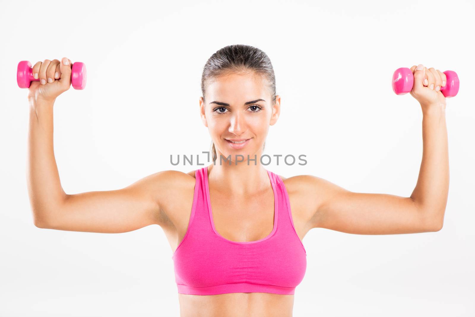 Portrait of a young beautiful woman exercising with dumbbells. She is practicing upper body muscle group.