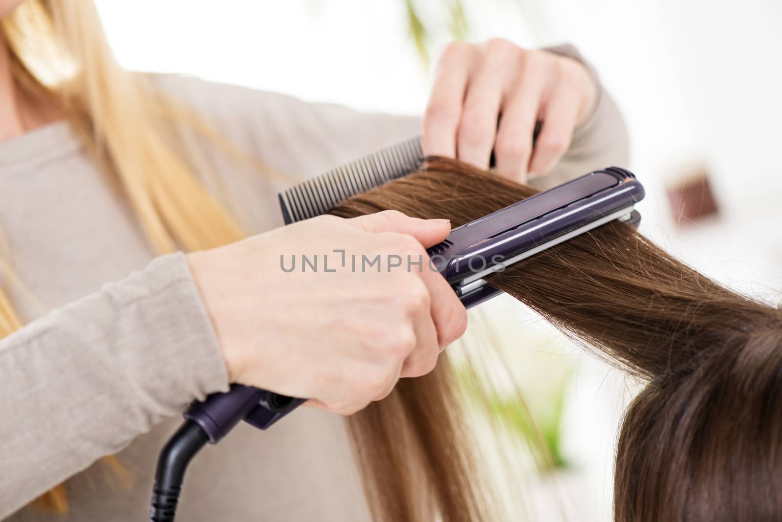 Hairdresser straightening long brown hair with hair irons.