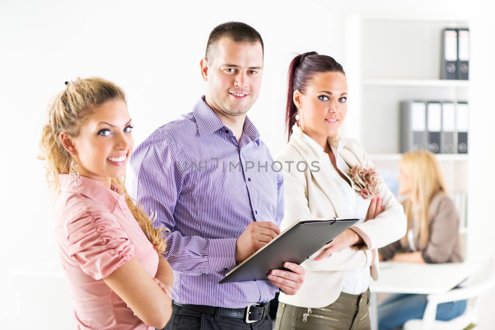 Three smiling co-workers standing in the office with crossed arm and looking at the camera.