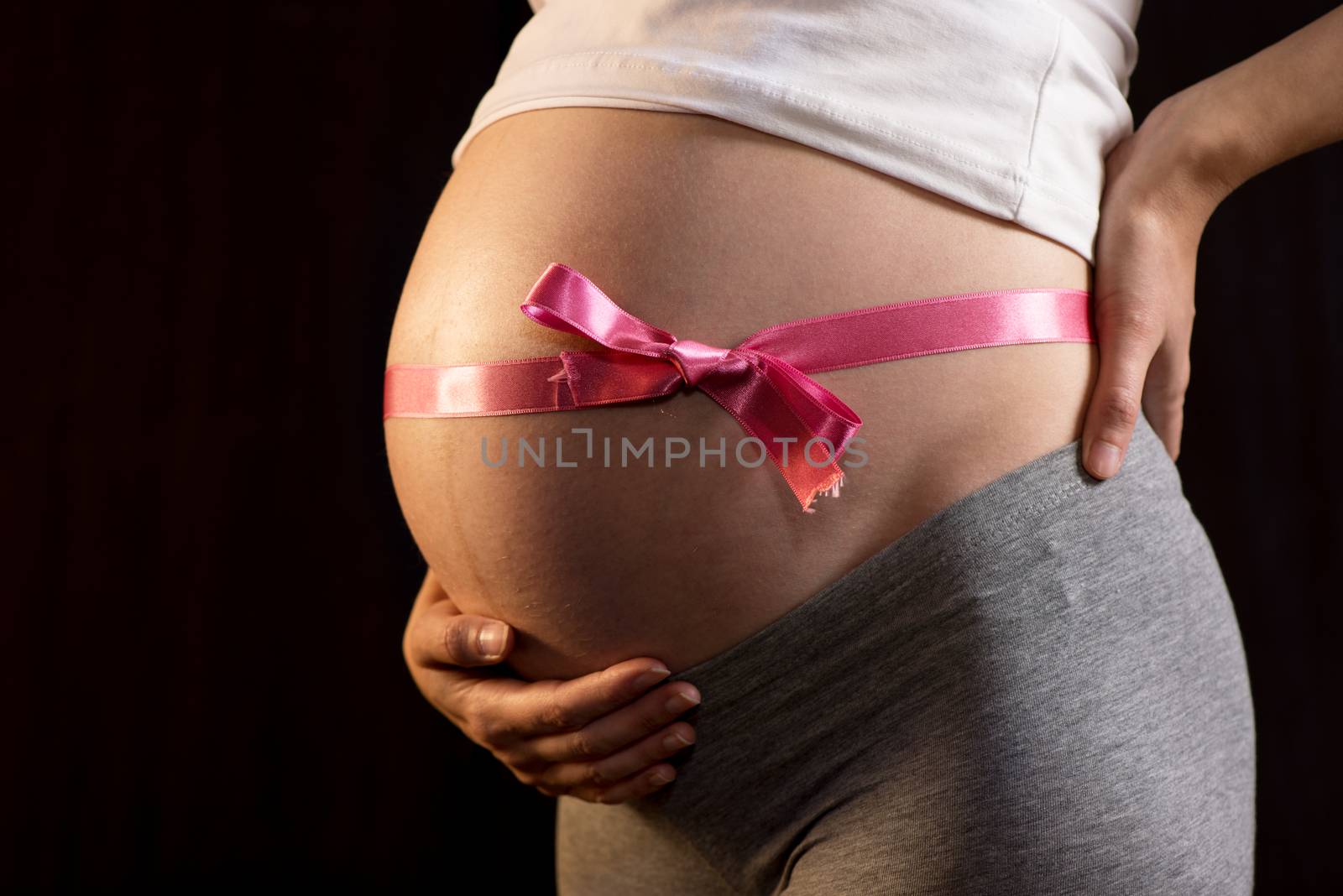 Pregnant woman on black background with ribbon on her belly.