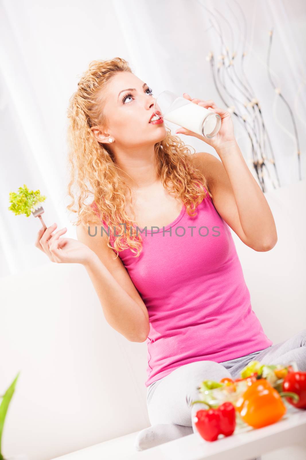 Beautiful young woman drink yogurt and holding salad with fork