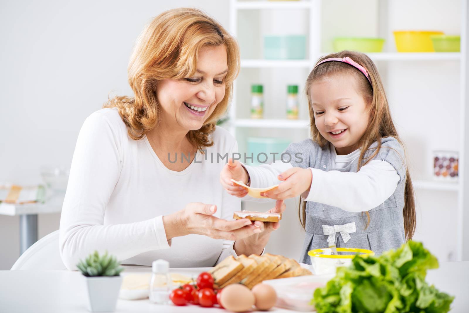 Beautiful happy grandmother and her cute granddaughter making a Sandwich in the kitchen.