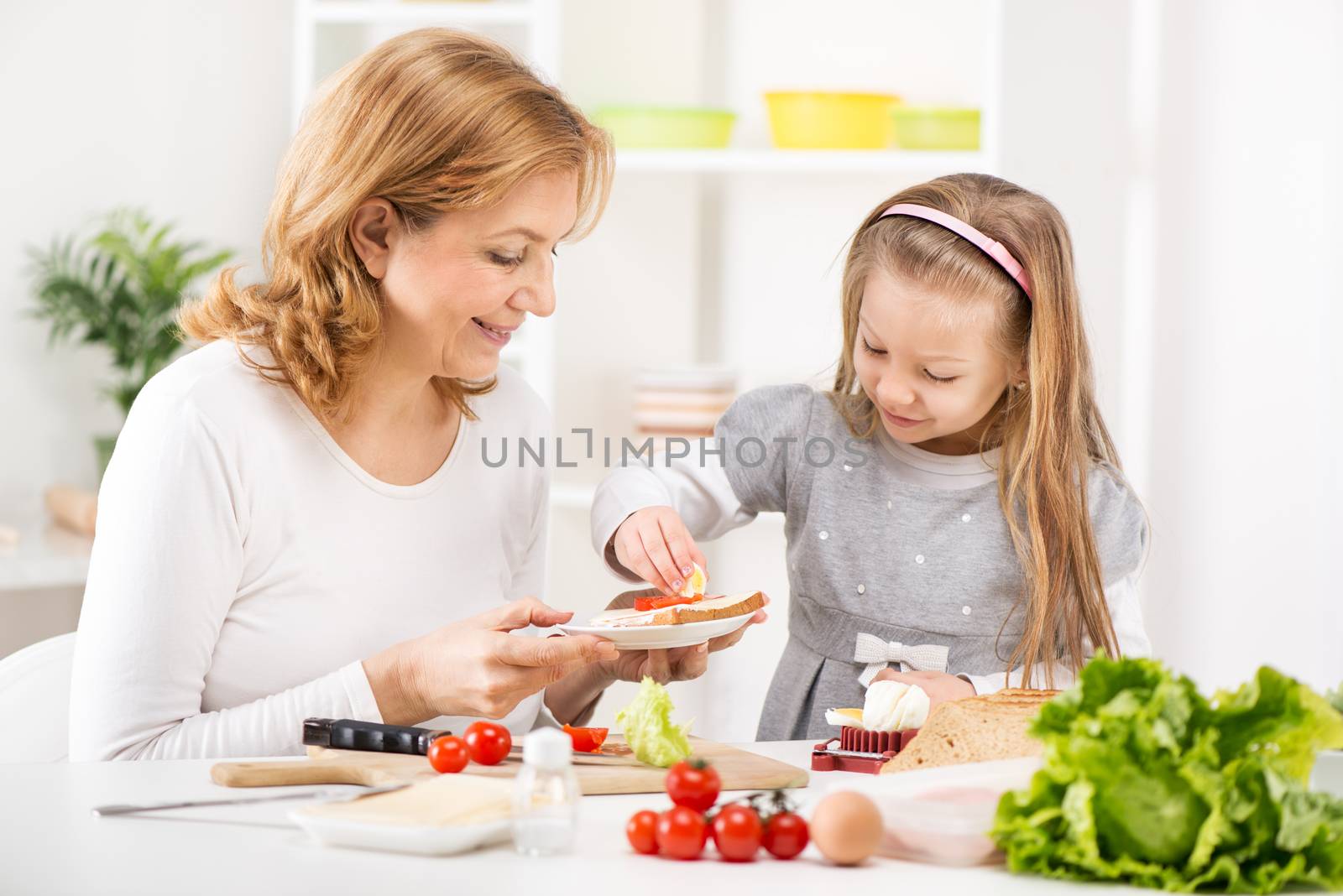 Cute little girl with Grandmother making a Sandwich in the kitchen.