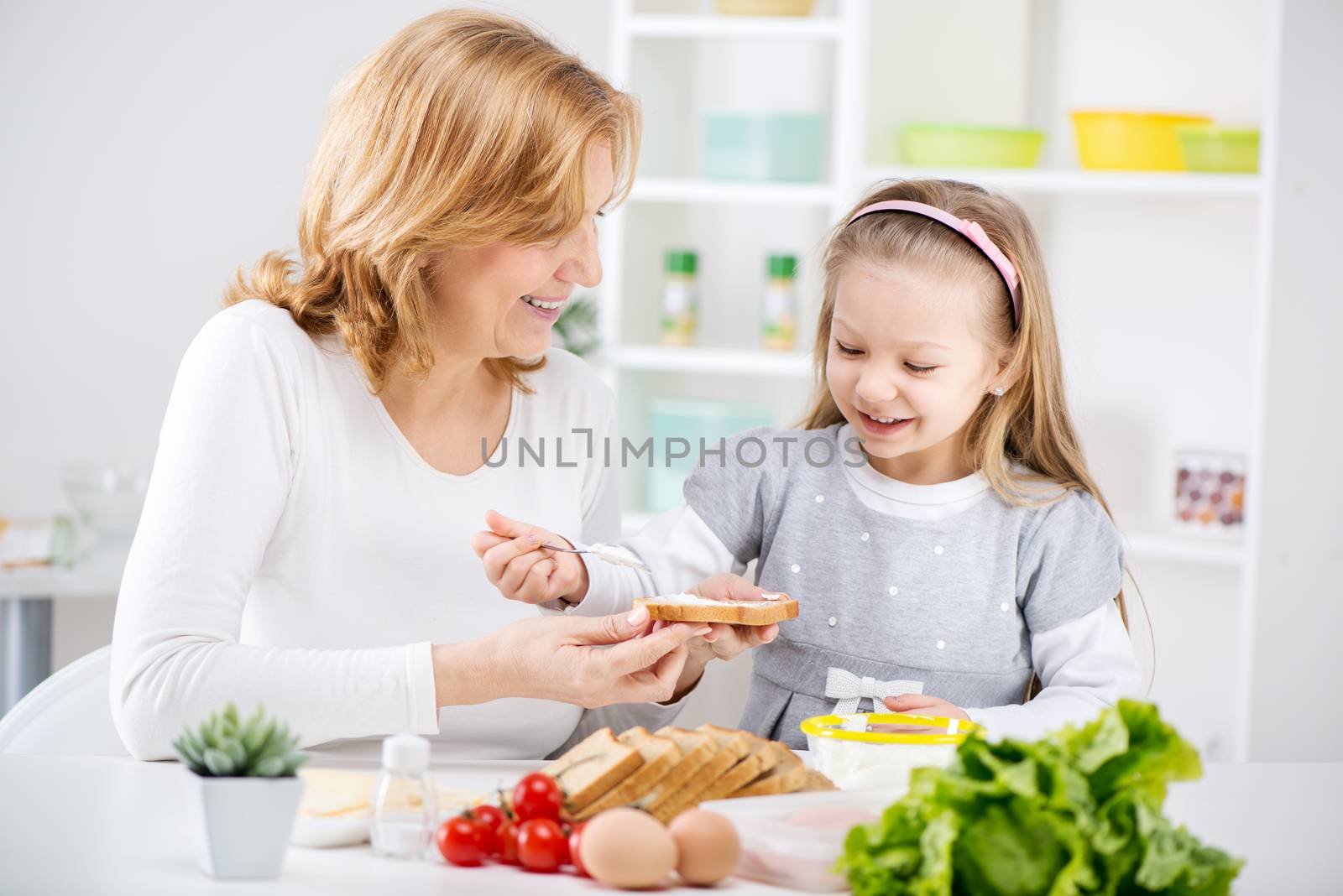 Beautiful happy grandmother and her cute granddaughter making Sandwich in the kitchen.