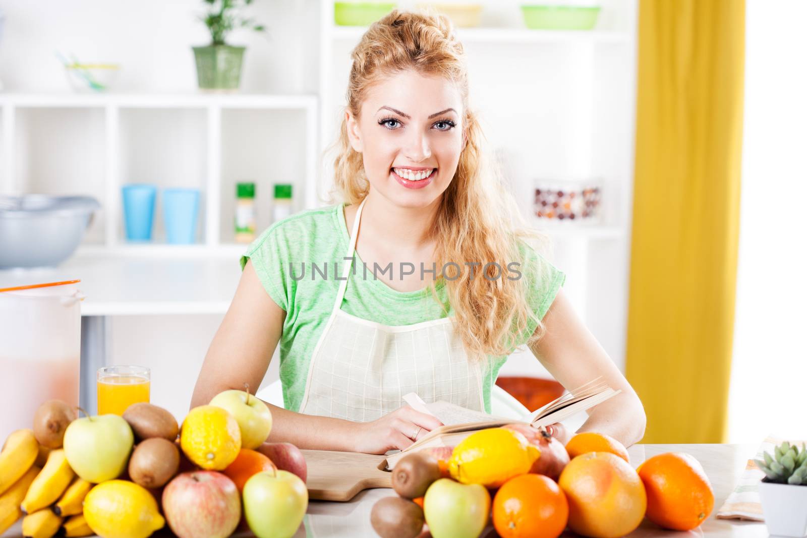Beautiful young woman reading cookery book in a kitchen. Looking at camera.