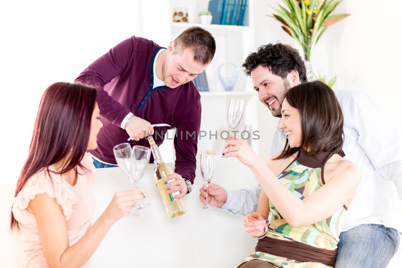 Group of happy friends sitting and drinking White Wine at Home Interior.