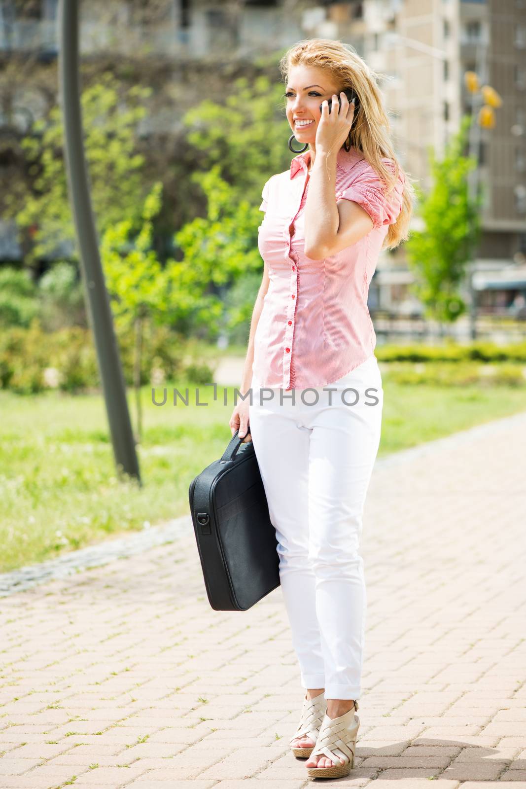 Beautiful young woman talking on phone and walking in the park.