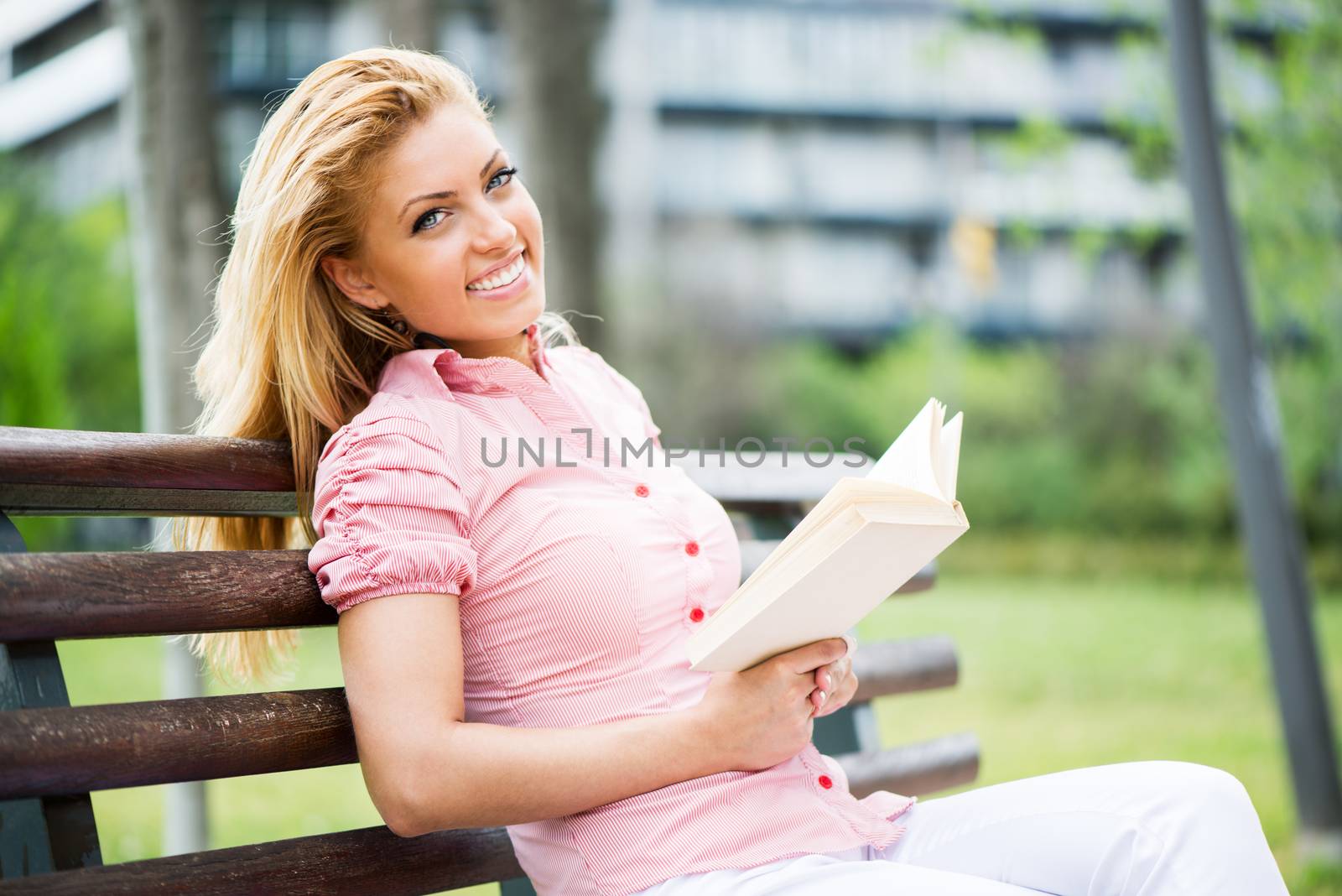 Young Beautiful Woman Reading Book In The Park, and sitting on the Park Bench.