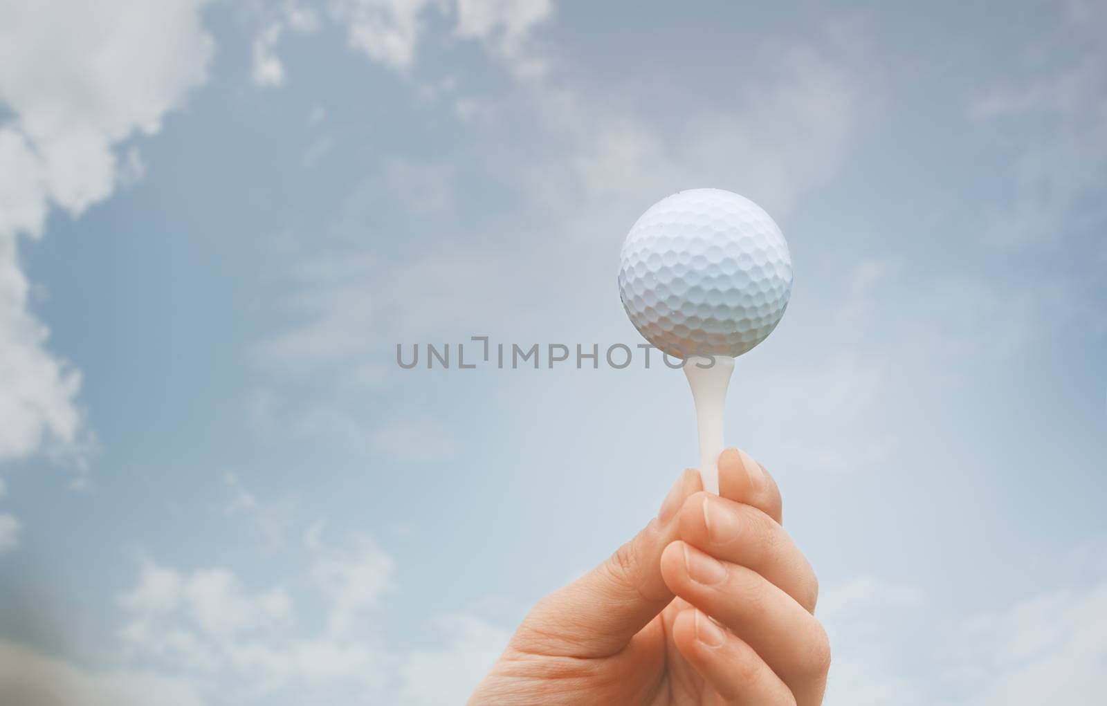 Human hand holding galf ball against the sky background