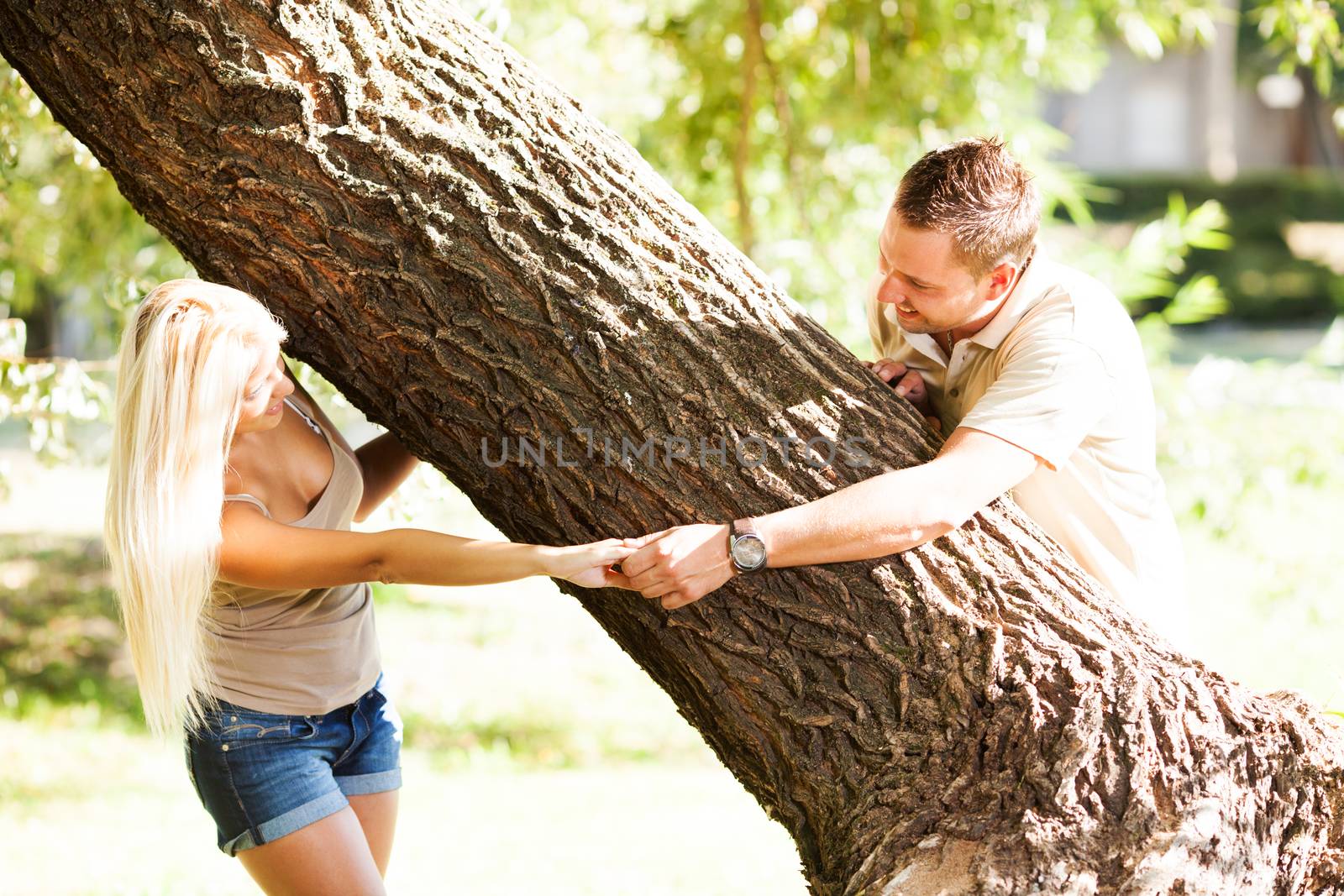 Beautiful, happy romantic couple in the park and holding hands around the tree.