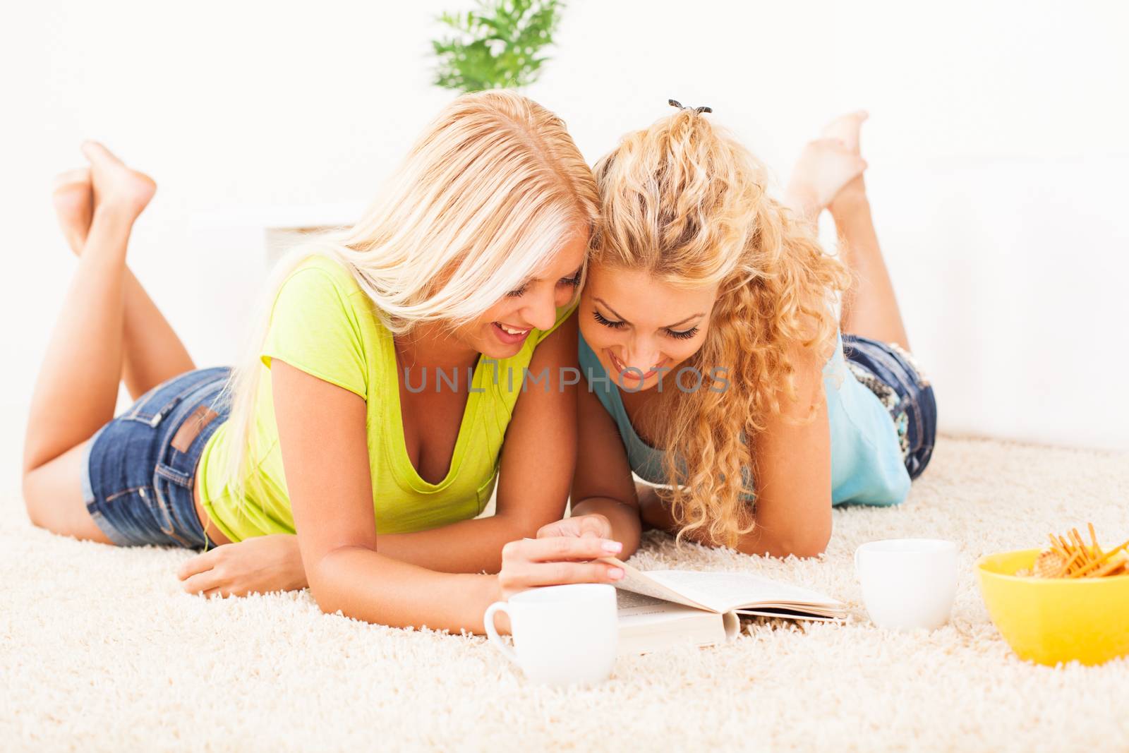 Two Beautiful girls lying in the carpet and reading a book.