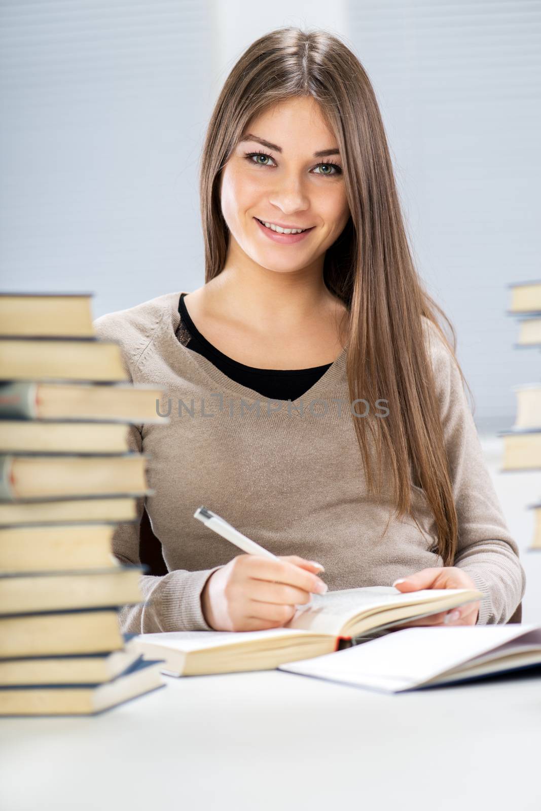 Beautiful Student girl sitting with many books and marking text what need to learn. Looking at camera.