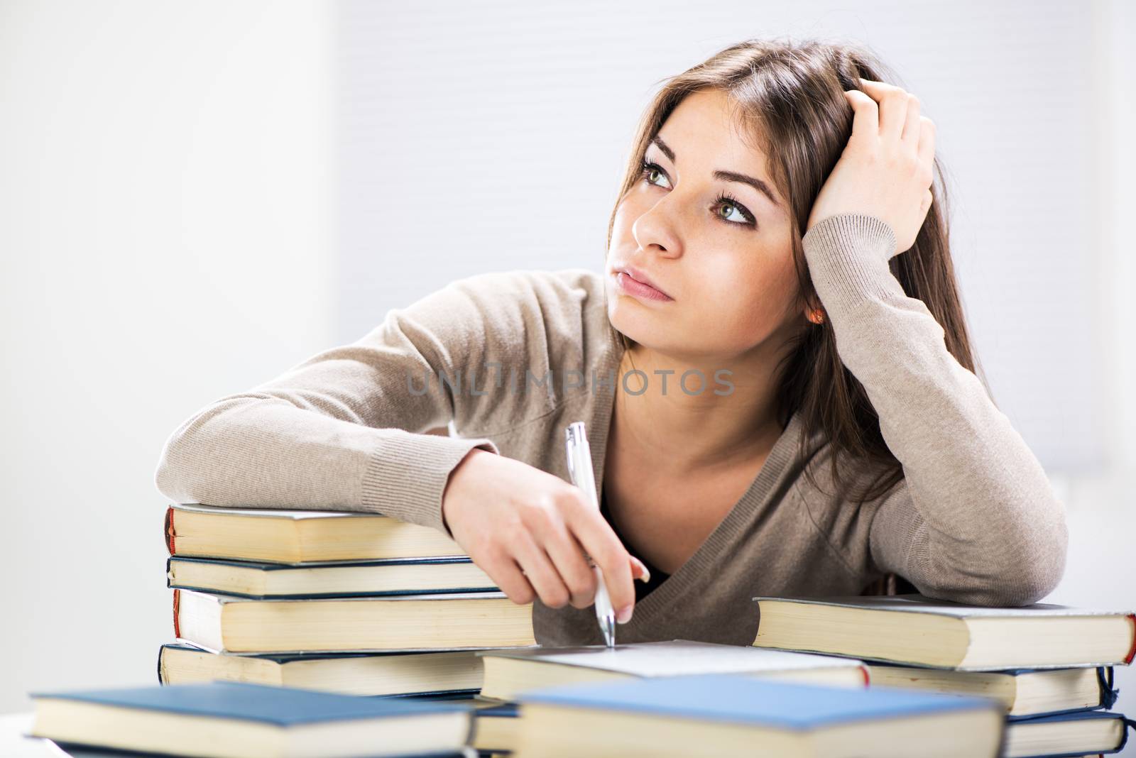 Tired student sitting with many books, with her head in hand.