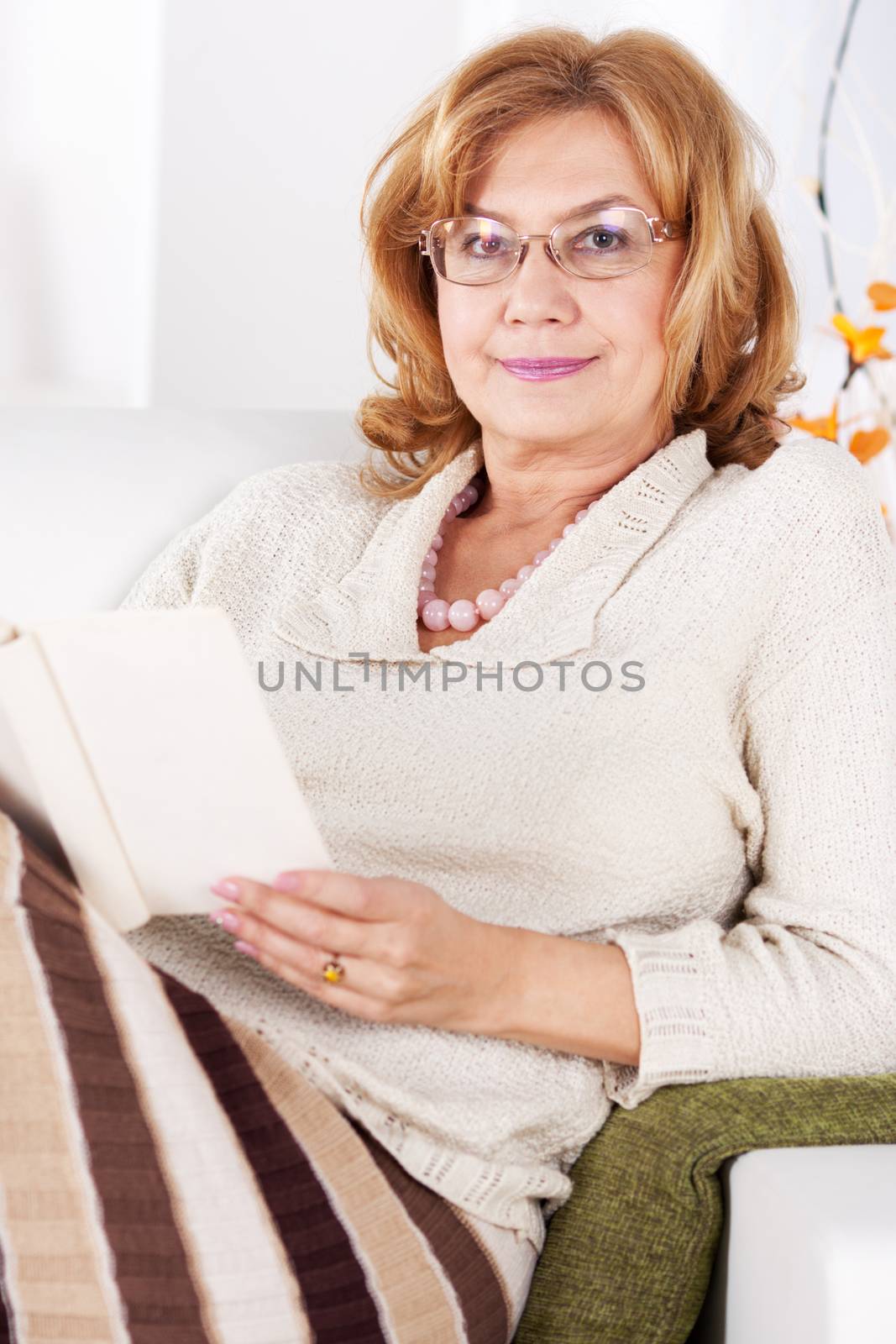 Senior woman sitting in living room and reading book.