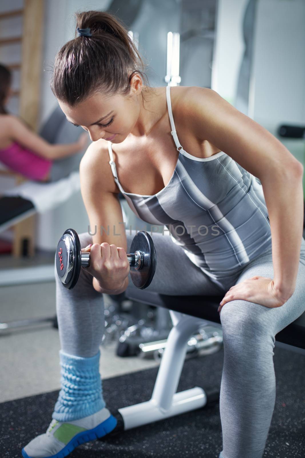 Cute Sporty young woman doing exercise in a fitness center. She is working exercises to strengthen her biceps.