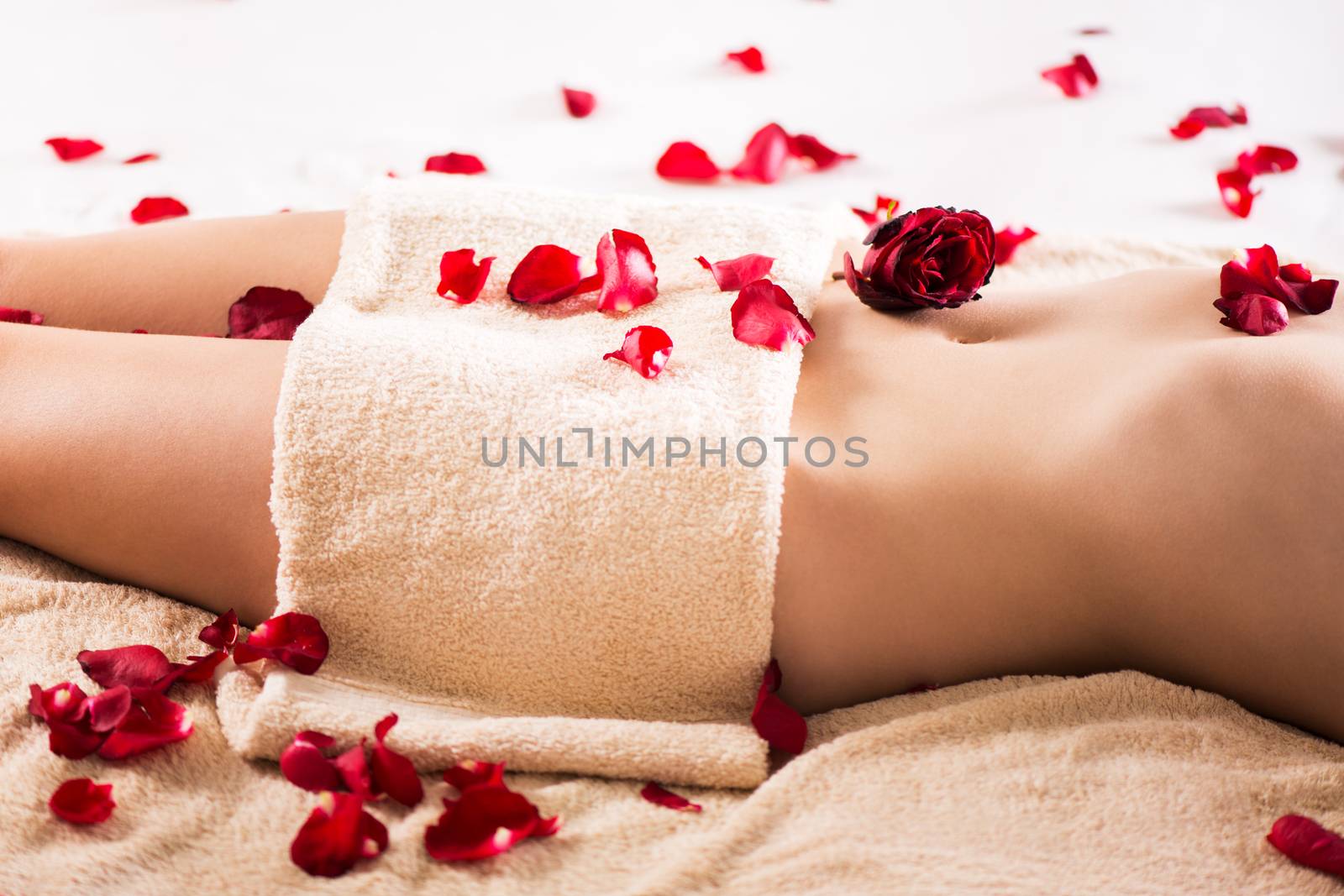 Beautiful female body covered with a towel and petals of roses.