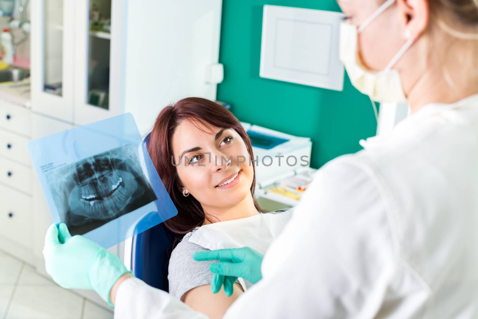 Young female dentist showing to the patient X-ray picture in she`s office.