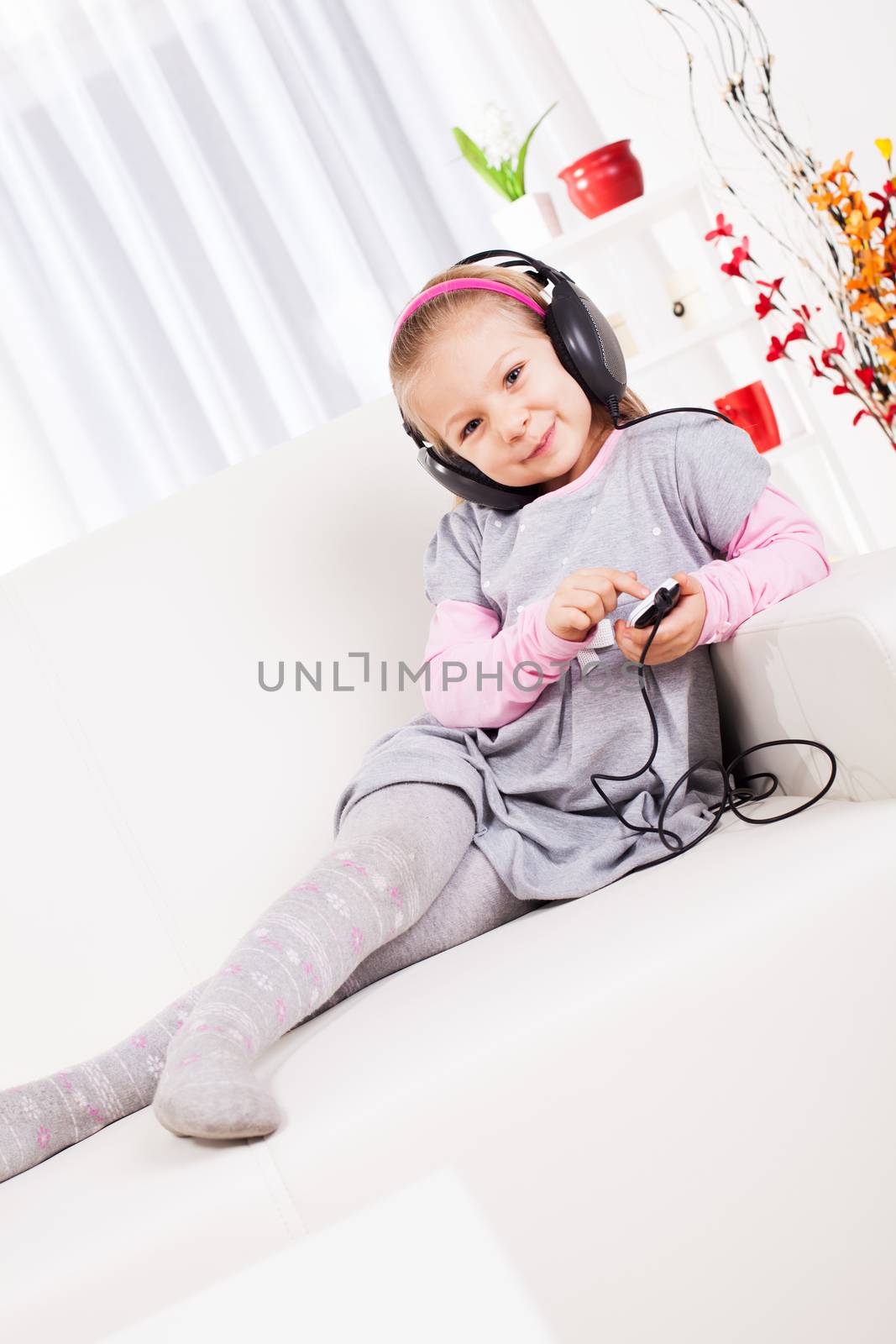 Cute little girl listening music with headphones at home.